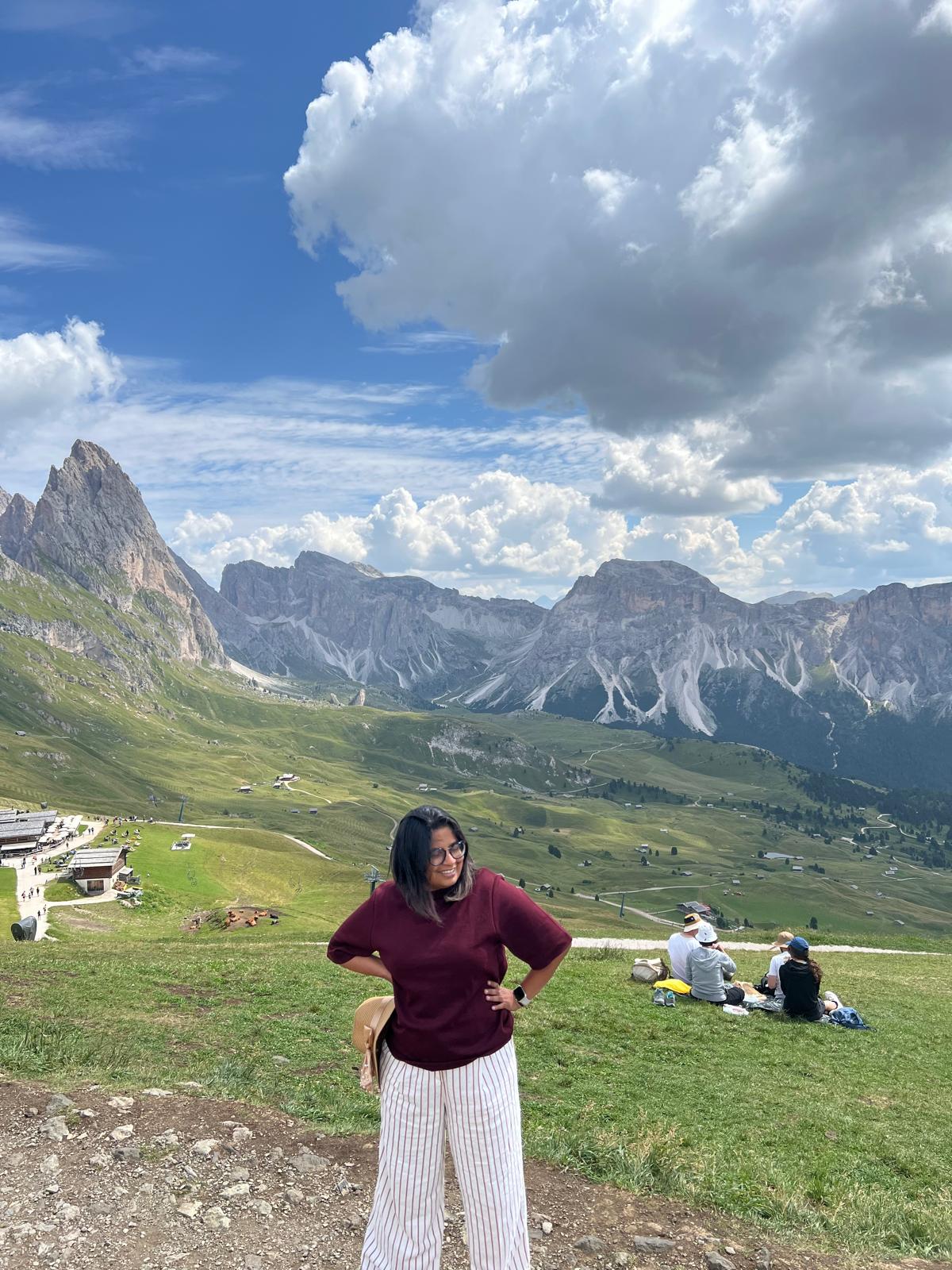 Nilima in the Dolomites beneath a blue sky and white clouds.